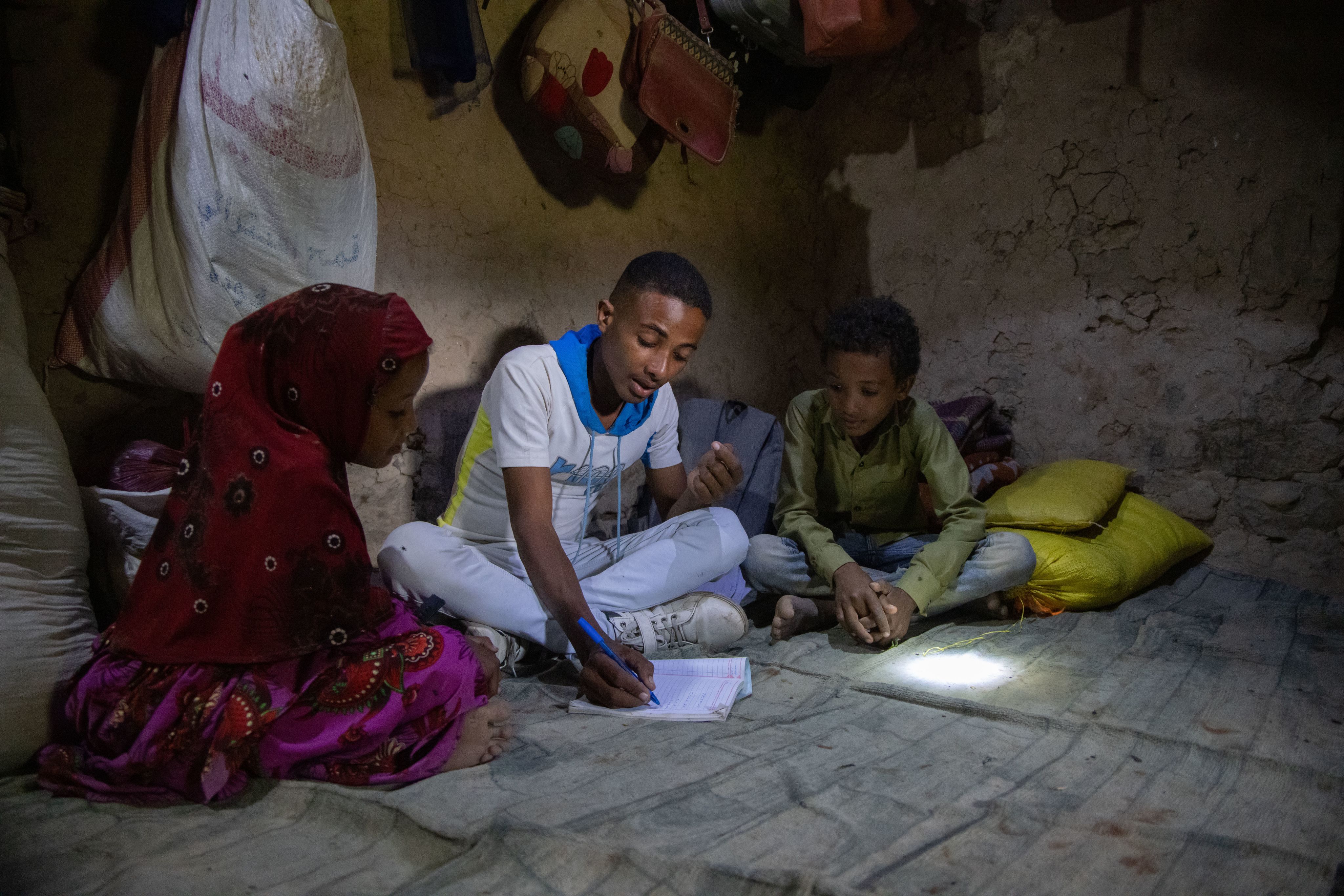 Munadhel sits with two of his siblings, Sarah* and Omar*, at home, helping them with their homework.